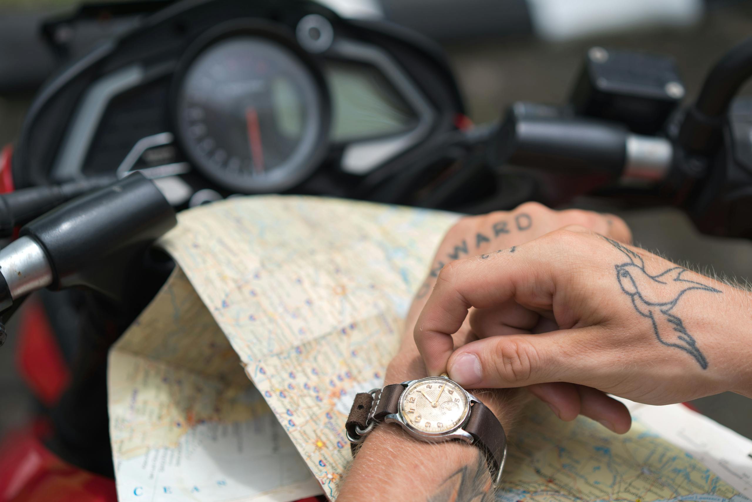 Close-up of tattooed hands using a map on a motorcycle journey.